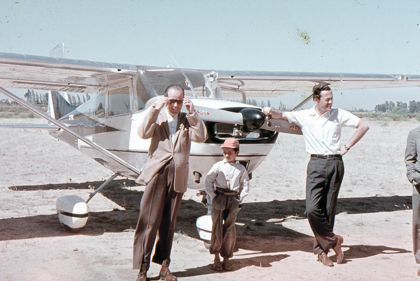 Dos hombres y un niño junto a una avioneta en un campo circa. 1965