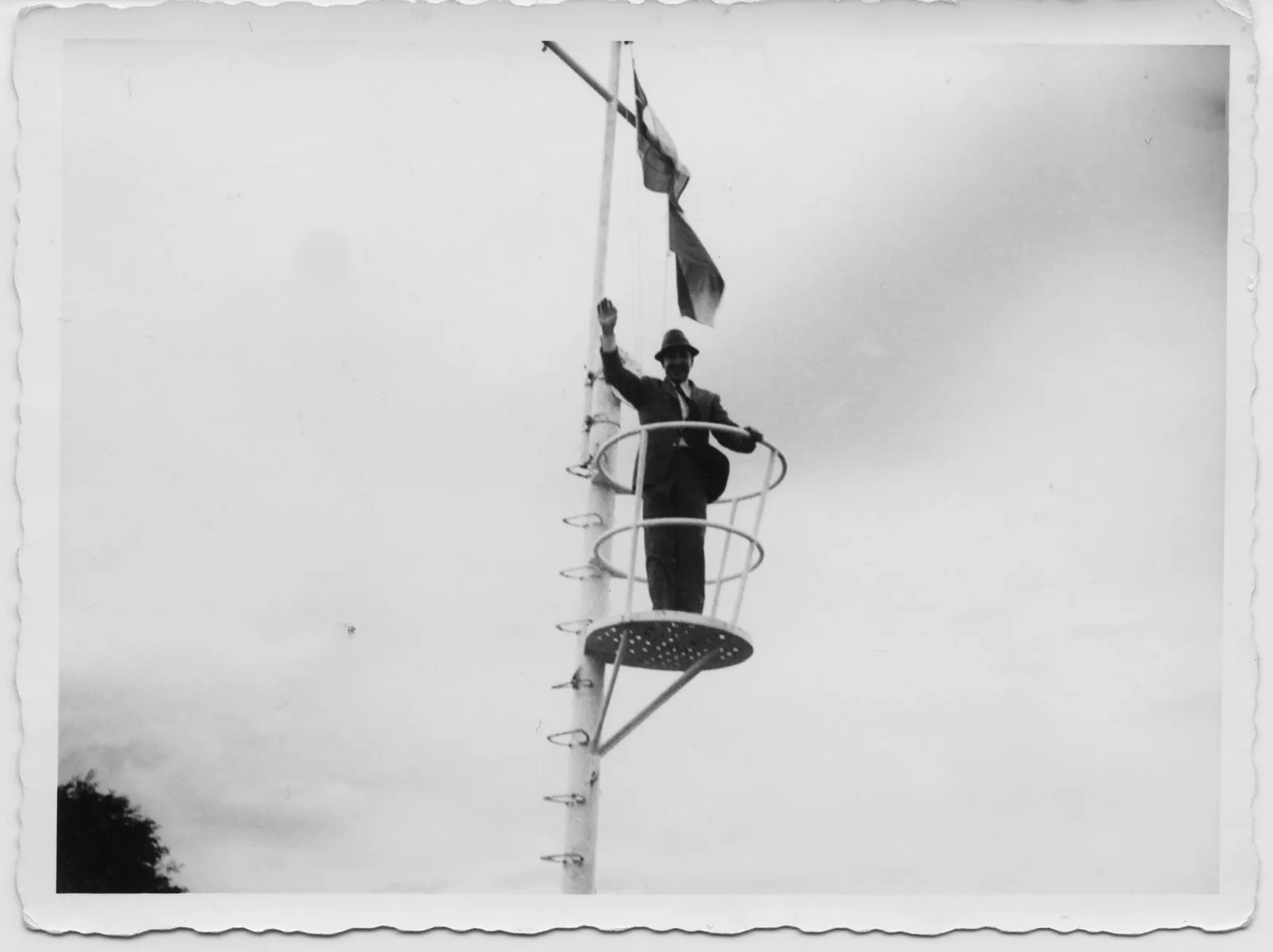Hombre saluda en estructura metálica con bandera chilena, ca. 1975